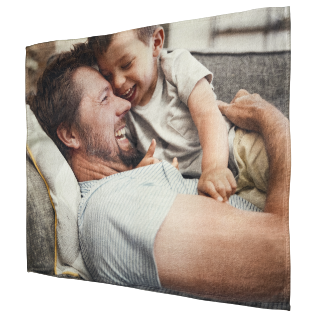 A photo of a man and a child cozying up under a Super Plush Fleece Blanket from Fuji Personalized Photo Products on a couch.