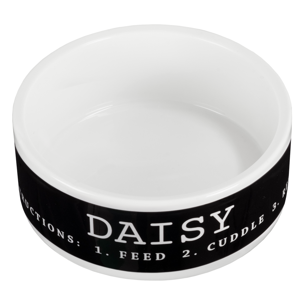 A personalized white and black ceramic pet bowl by Fuji Personalized Photo Products for small dogs with the name "Daisy" and the words "Instructions: 1. Feed 2. Cuddle" printed on it.