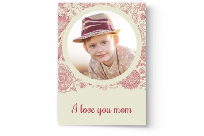 A Photo Book Press Mother’s Day card featuring a circular framed photo of a smiling child wearing a hat, with the text "I love you mom" printed below.
