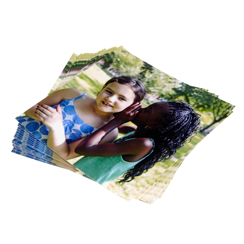 A girl is holding a girl's hand in front of a pile of Fuji Personalized Photo Products Small Format Prints.