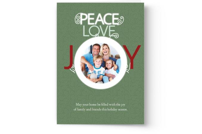 A Custom Photo Christmas Card with the words "peace, love, joy" and a photograph of a smiling family in a circular frame from PhotoBook Press.