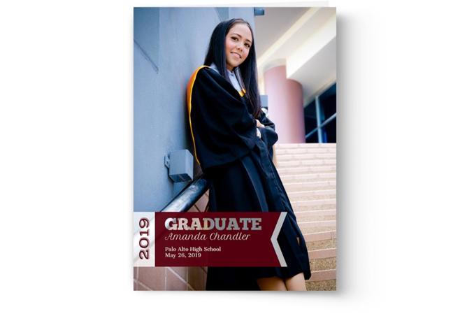 A woman in a graduation gown, personalized for her Photo Book Press graduation announcement cards and invitation, is leaning against a wall.