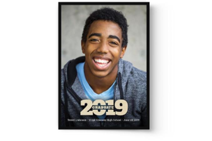 A photo of a young man smiling in a Photo Book Press custom printed graduation announcement card, in front of a black frame.
